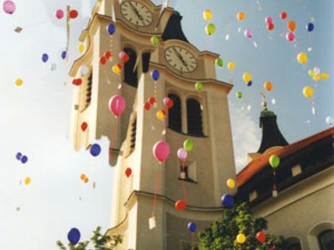 Luftballons steigen vor einem Kirchturm in den Himmel