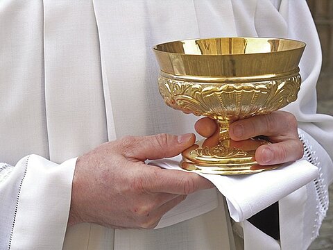 Man sieht einen Ministranten, der einen goldenen Kelch hält.