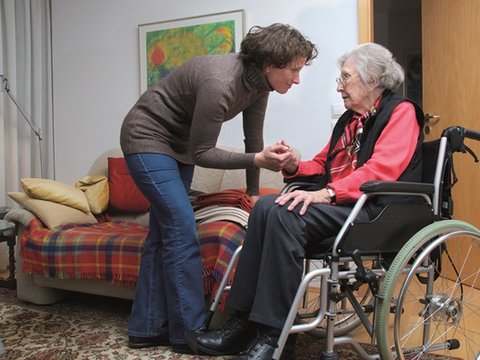 Eine Frau hilft einer älteren Dame im Rollstuhl.