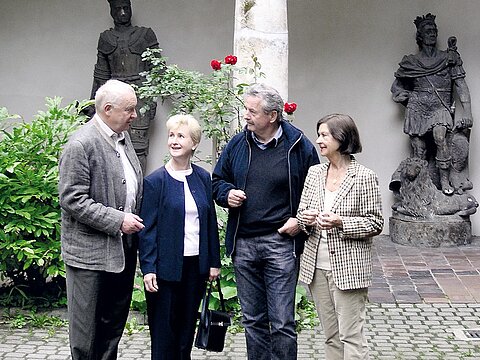 Vier ältere Personen stehen in einem Innenhof zusammen und sprechen miteinander.